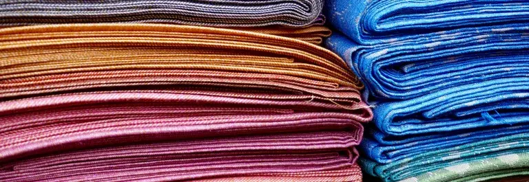 A pile of colourful folded textiles © Pexels