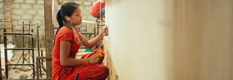 Woman weaving textiles in a red outfit and brick background